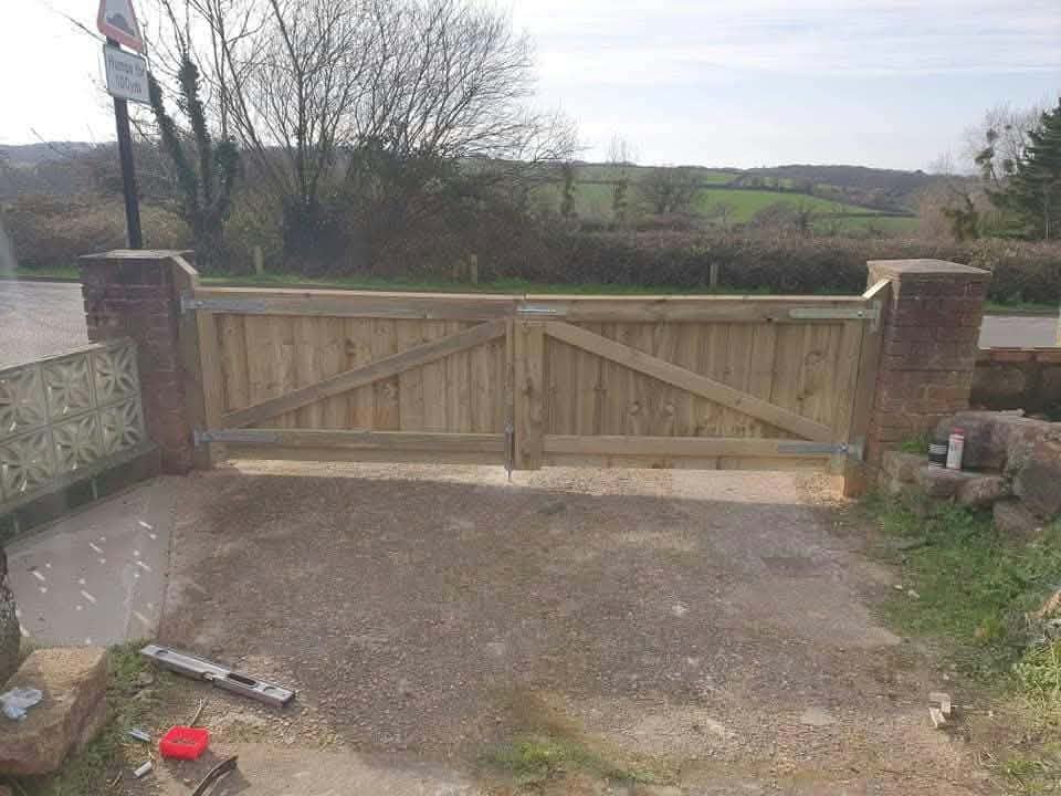 A pair of wooden driveway gates hung between brick pillars, with fields beyond