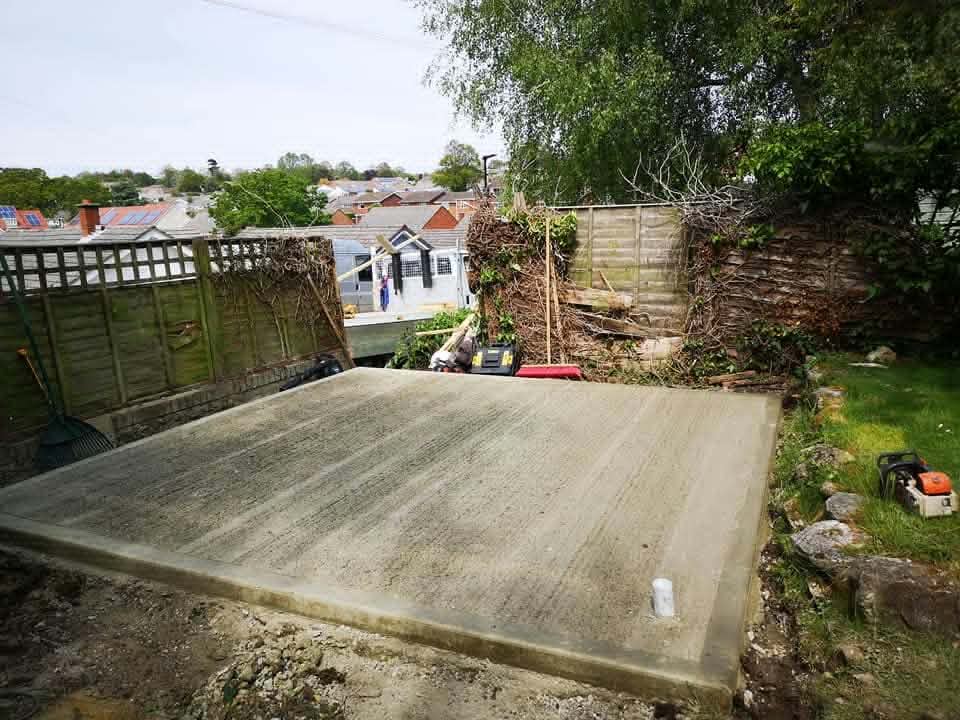 A new concrete shed base laid in a cleared corner of a garden