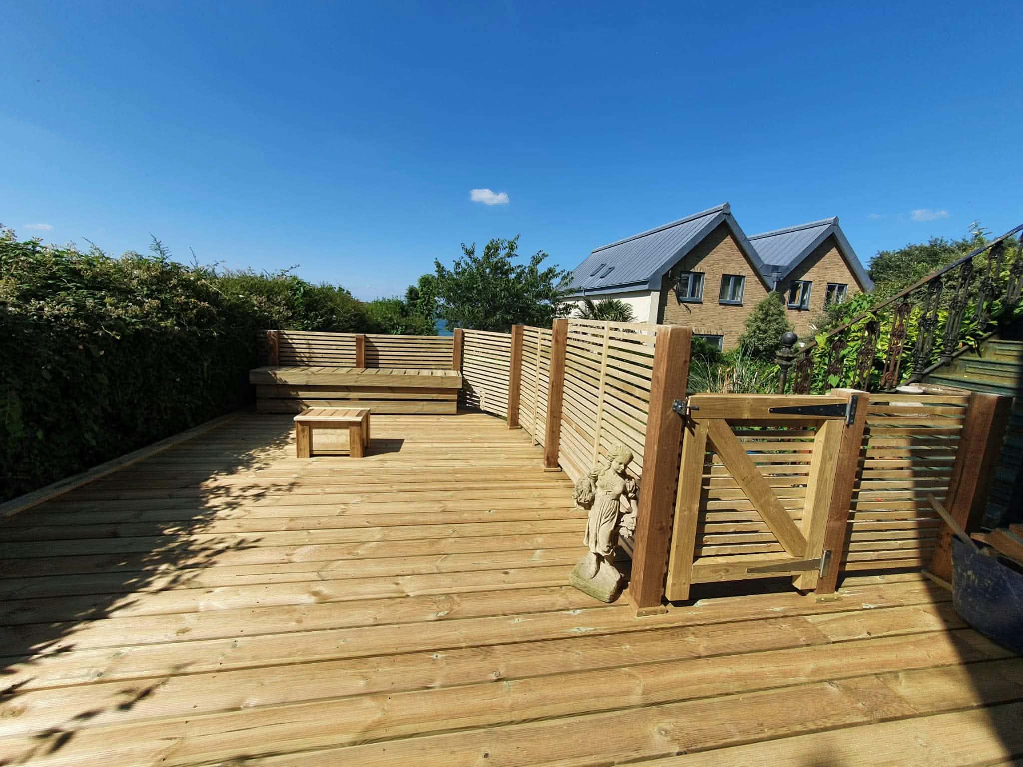 A new timber deck with built-in bench, slatted screens and a matching gate under a blue sky