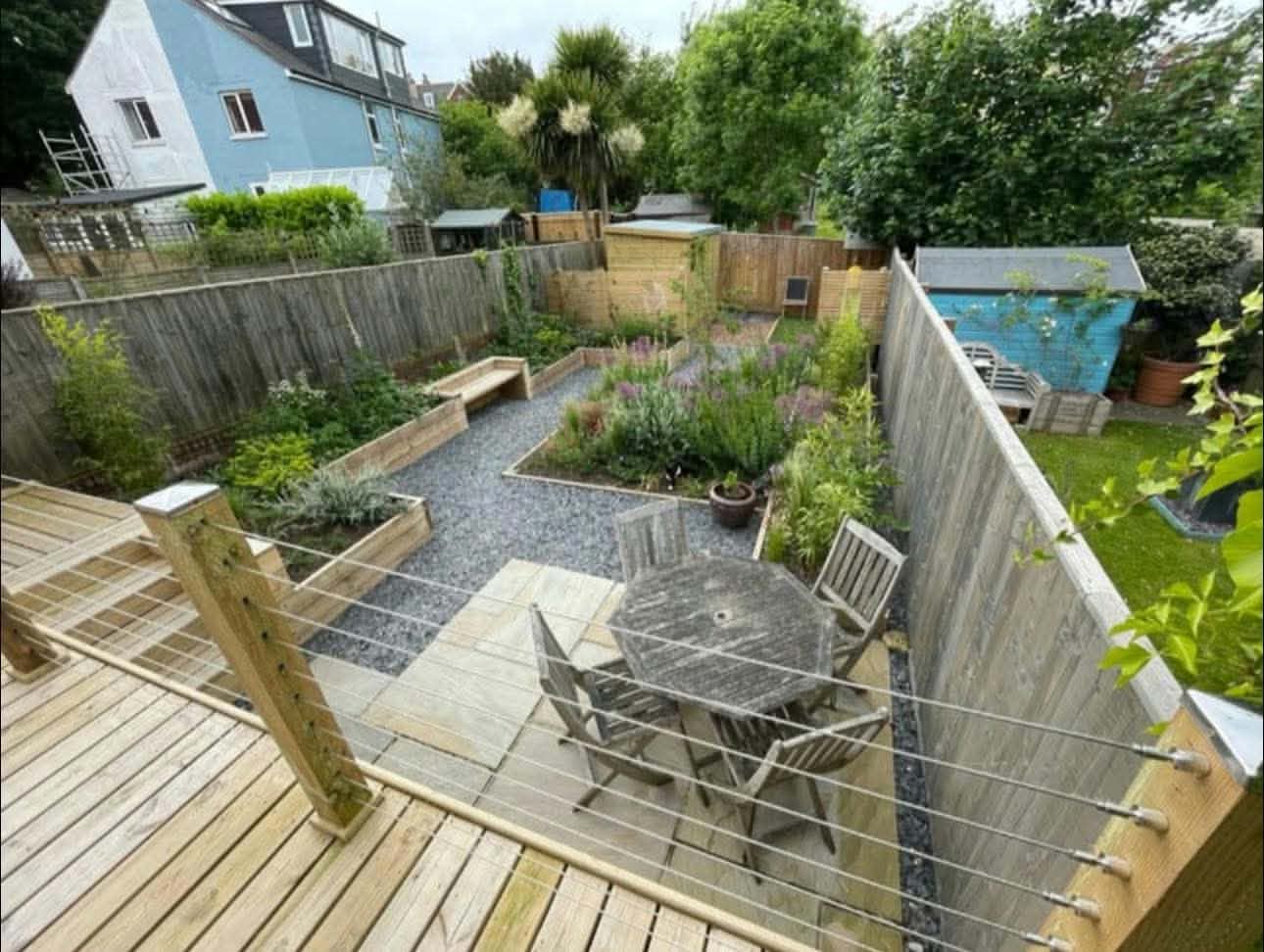 A terraced back garden with timber decking, a gravel seating area and planted raised beds
