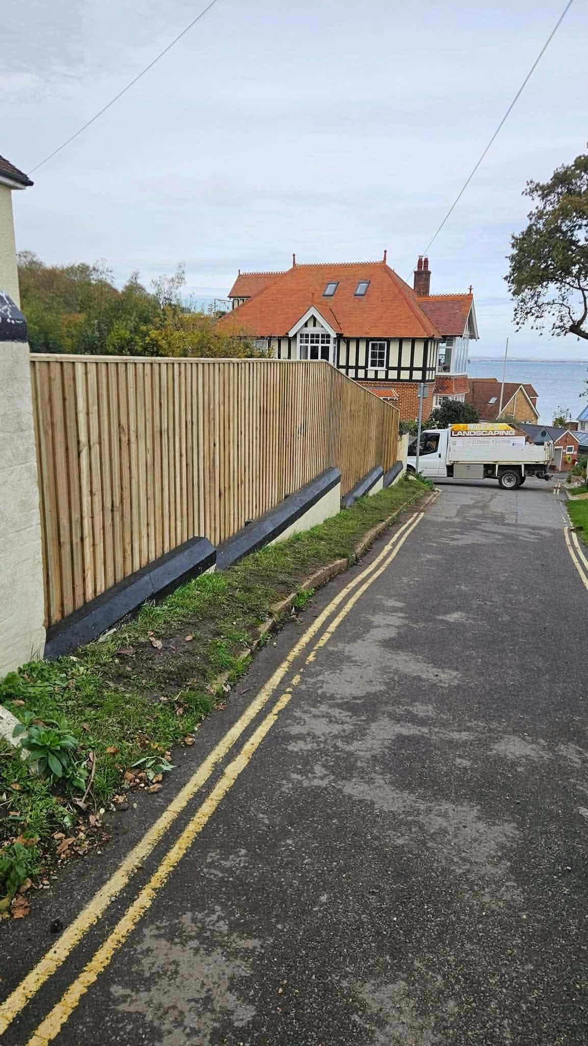 A long close-board fence running down a lane towards the sea