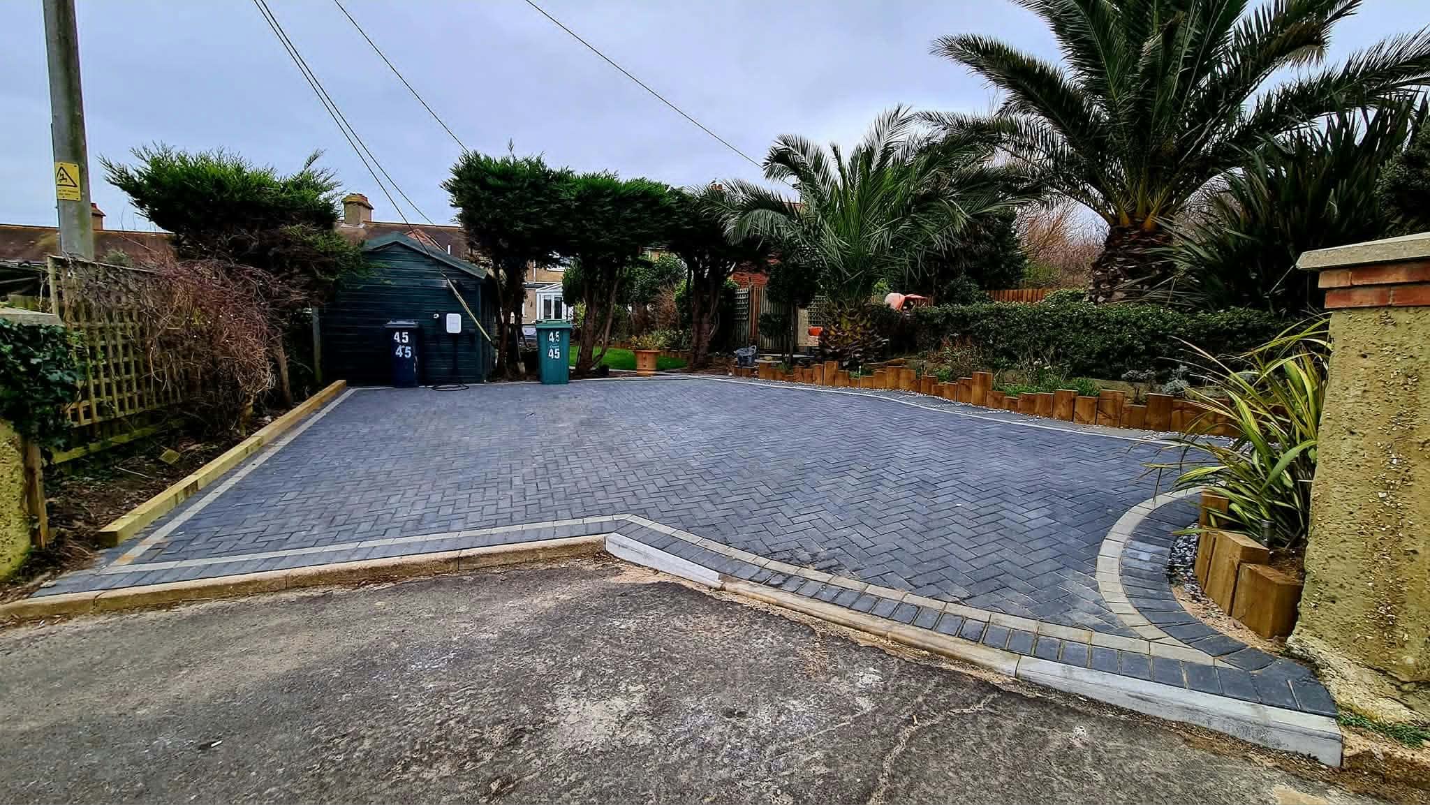 A new grey block-paved driveway with light kerb edging, framed by palm trees