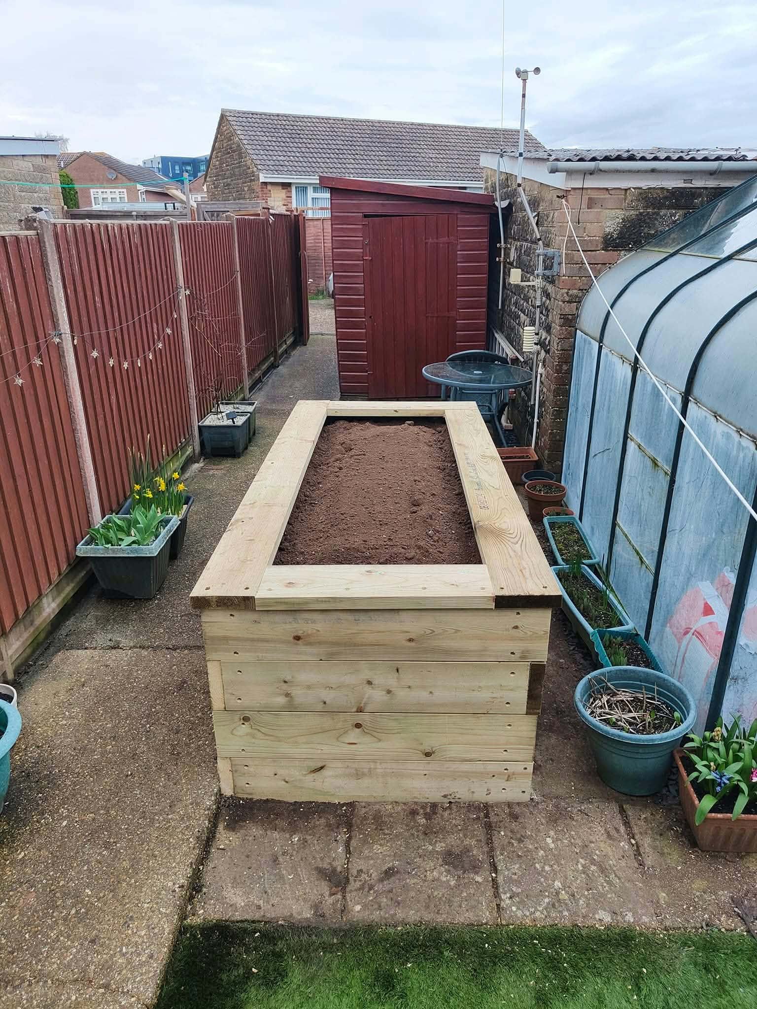 A tall timber raised planter filled with soil on a garden path