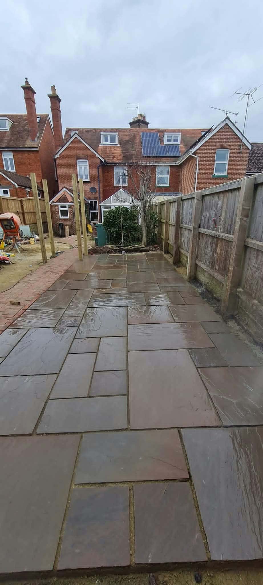 A long sandstone patio running down a terraced back garden beside a new fence