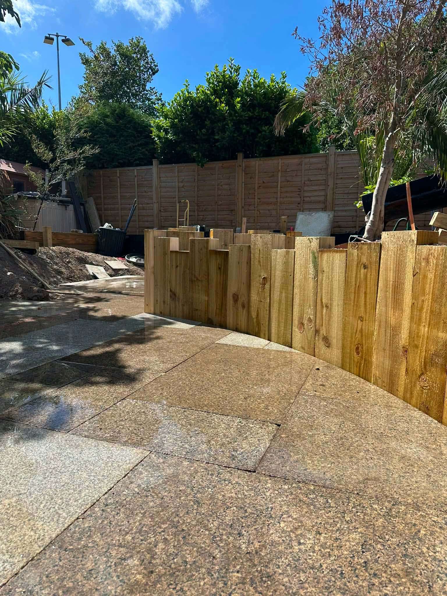 A curved wall of upright timber sleepers beside a new patio